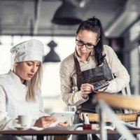 Kvinnelig kokk og servitør med ipad og kalkulator. Foto